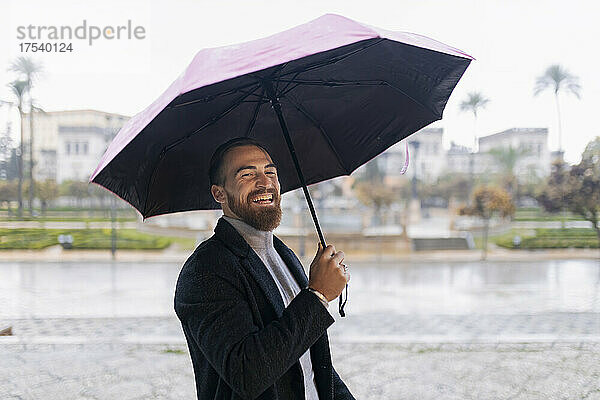 Cheerful young man with umbrella enjoying rain