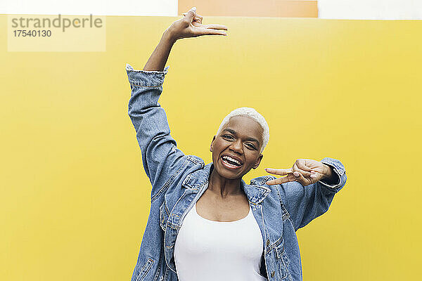 Happy woman making peace sign gesture against yellow background