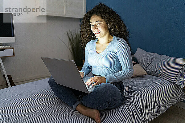 Young woman using laptop sitting on bed at home