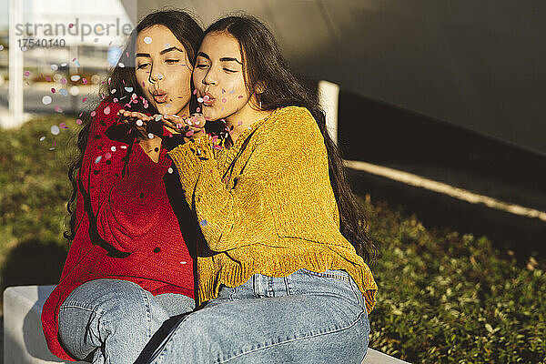 Playful sisters blowing colorful confetti on sunny day