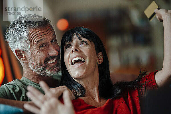 Cheerful woman with credit card by man at home
