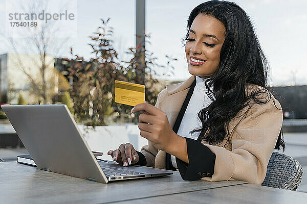 Lächelnde Geschäftsfrau mit Kreditkarte beim Online-Shopping am Laptop