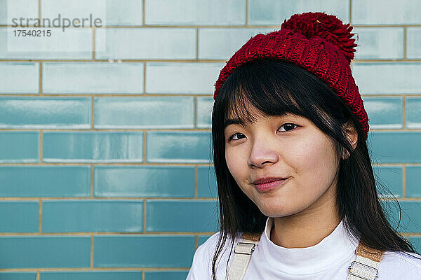 Smiling woman wearing red knit hat in front of turquoise wall