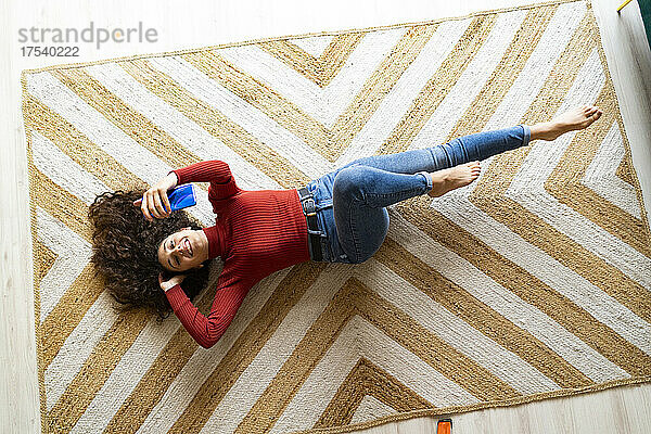 Woman taking selfie through mobile phone lying on carpet at home