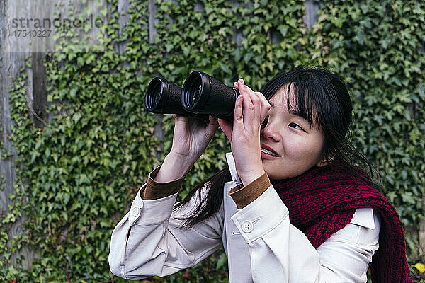 Smiling young woman looking through binoculars