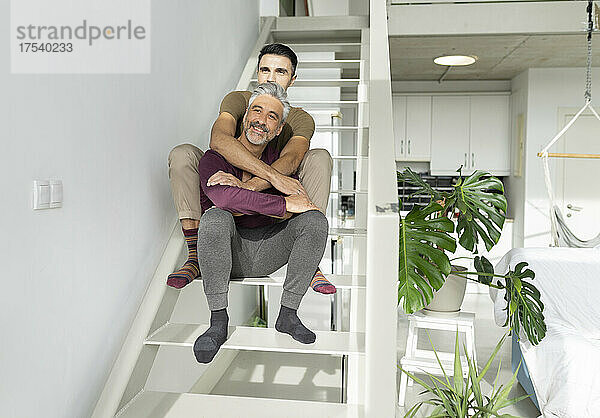 Smiling gay couple embracing on steps at home