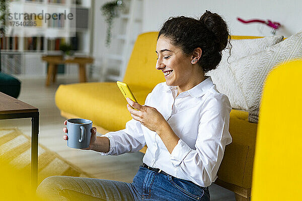 Smiling woman photographing coffee mug through smart phone at home