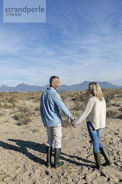 Mann und Frau halten sich an den Händen und stehen an den Dünen