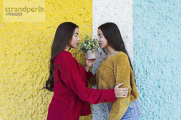 Twin sisters smelling flowers together by colorful wall
