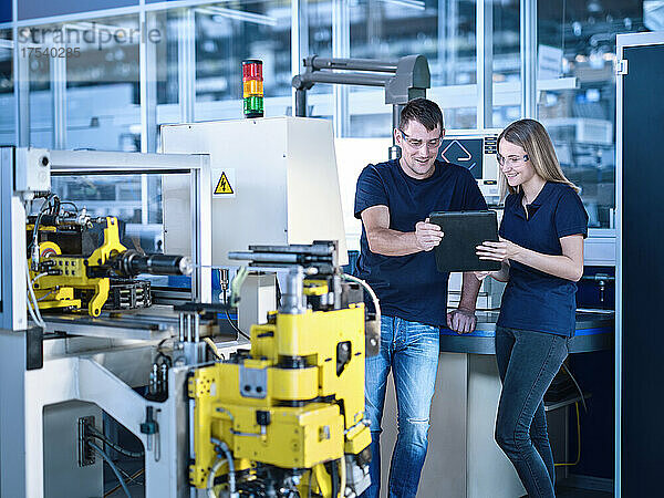 Lächelnde Ingenieure diskutieren am Tablet-PC in einer automatisierten Fabrik