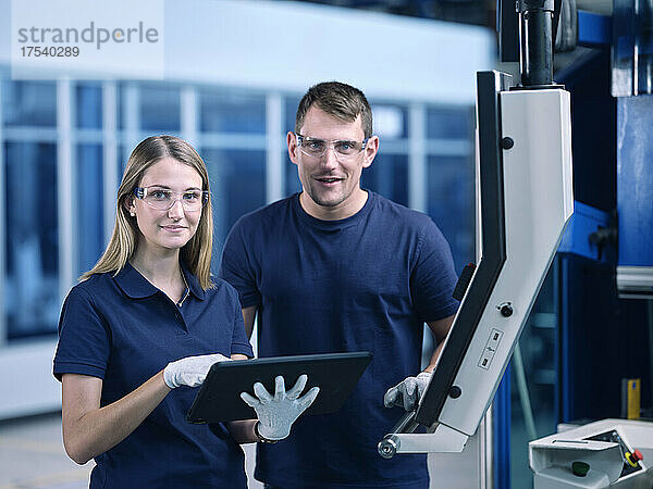 Ingenieure mit Schutzbrille und Tablet-PC in der Nähe von Maschinen in der Industrie