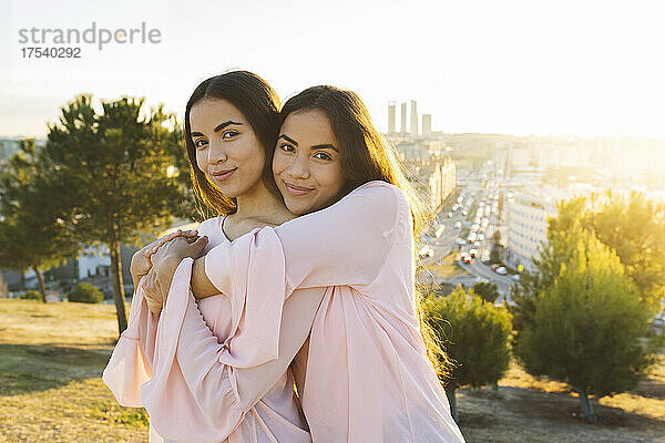 Smiling sisters embracing each other in park at sunset