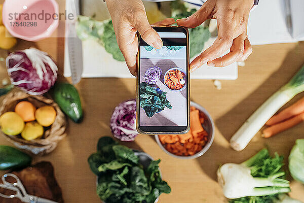 Woman photographing fresh vegetables using smart phone at home