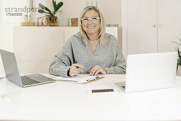 Lächelnde Geschäftsfrau mit Laptops auf dem Schreibtisch am Arbeitsplatz