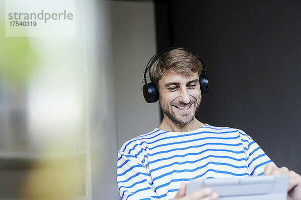 Lächelnder Geschäftsmann mit kabellosen Kopfhörern und Tablet-PC im Heimbüro