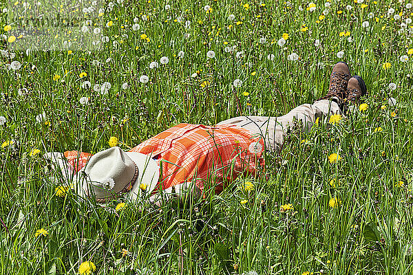 Man sleeping on grass with hat over face at meadow