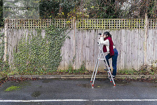 Woman standing on ladder looking through binoculars