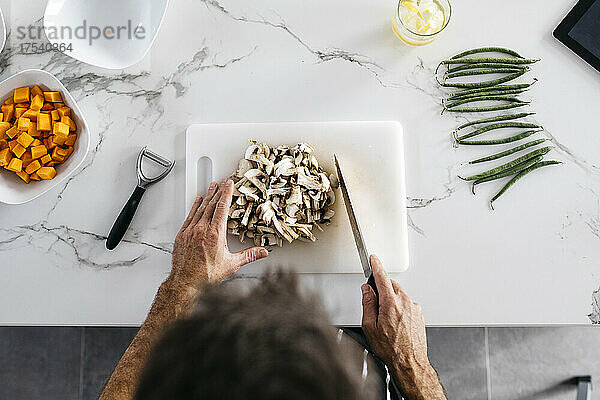 Man arranging chopped mushrooms on cutting board in kitchen at home