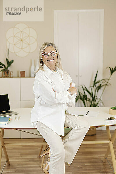 Smiling businesswoman sitting on desk at workplace