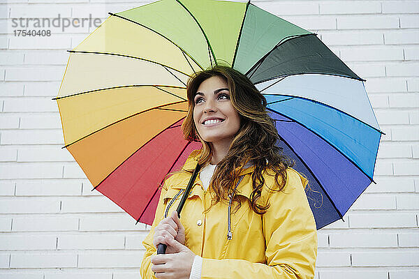 Nachdenkliche Frau hält Regenschirm vor der Wand