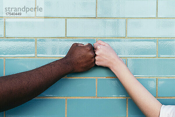 Multiracial friends giving fist bump on turquoise brick wall