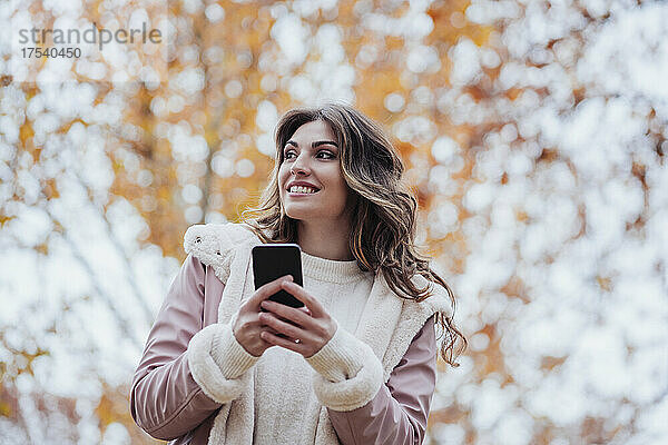 Lächelnde Frau hält Mobiltelefon im Park
