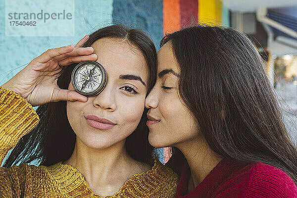 Young woman covering eye with compass by twin sister