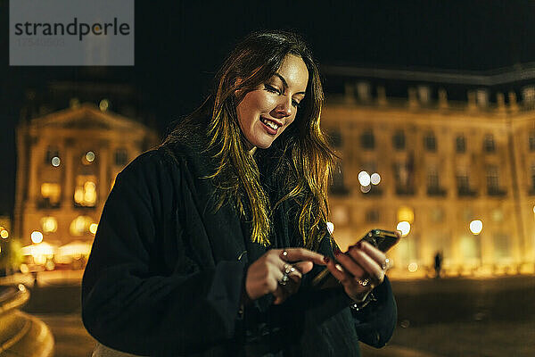 Smiling young woman using smart phone in city at night