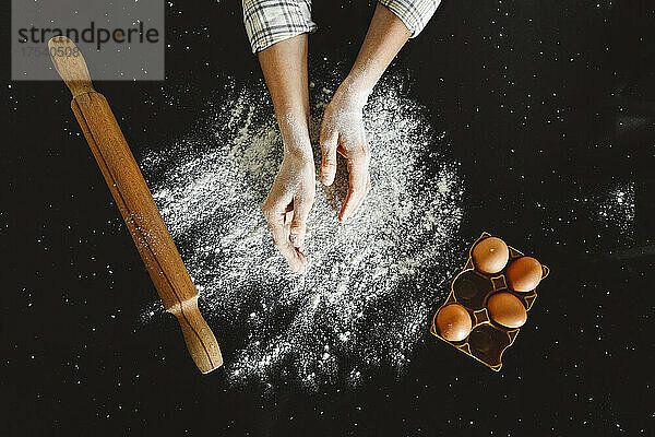 Frau bestäubt Mehl mit Eierablage auf schwarzem Hintergrund