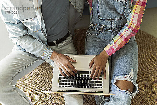 Young couple using laptop together sitting on carpet