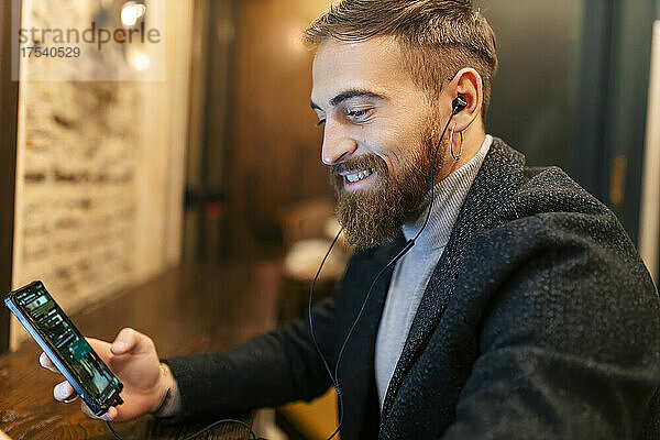 Happy young man using mobile phone and listening music through in-ear headphones