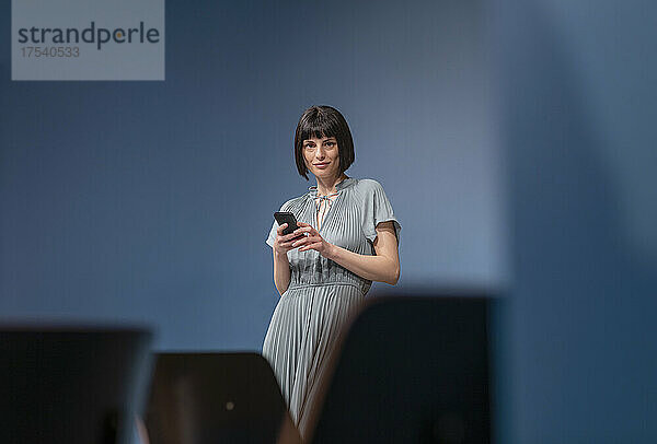 Confident businesswoman with mobile phone in office