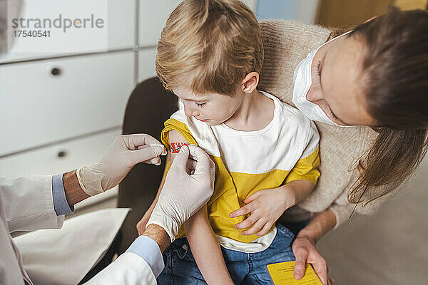 Junge bekommt vom Arzt nach der Impfung im Zentrum einen Verband