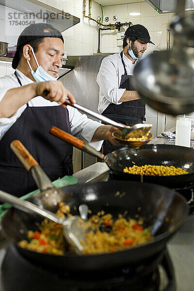Chefs with face mask preparing food at restaurant kitchen
