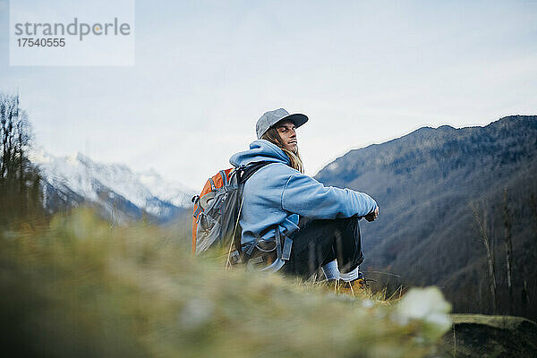 Mann mit Rucksack sitzt mit geschlossenen Augen auf dem Berg