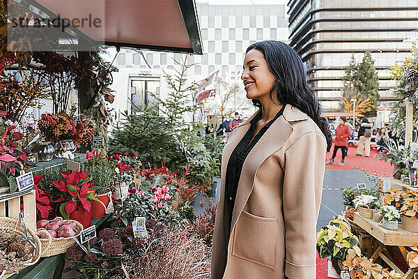 Lächelnde Frau mit Mantel im Blumenladen auf dem Weihnachtsmarkt