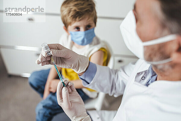Im Hintergrund in der Mitte bereitet der Arzt eine Impfinjektion für einen Jungen vor