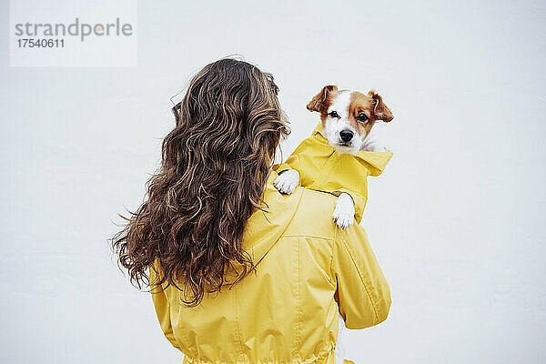 Woman with long brown hair carrying dog in front of white wall