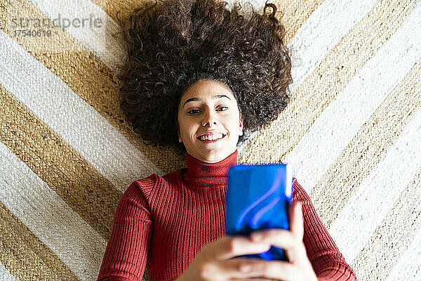 Frau benutzt Smartphone und liegt zu Hause auf dem Teppich