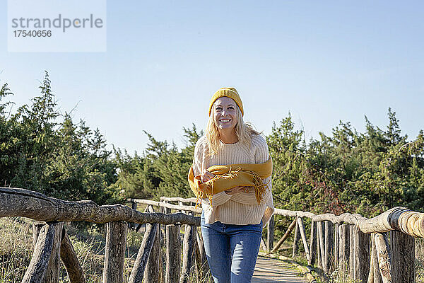 Lächelnde Frau mit Schal steht auf einer Holzbrücke