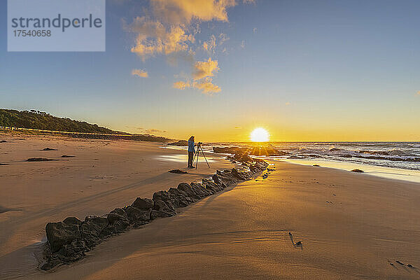 Female tourist taking photos on sandy coastal beach at sunrise