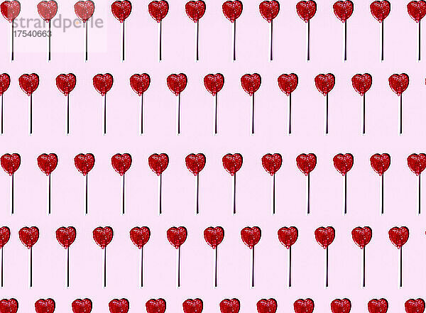 Pattern of heart shaped lollipops flat laid against pink background