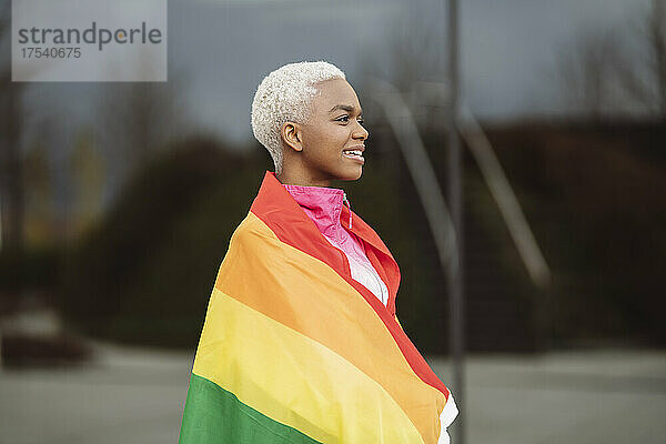 Smiling LGBTQIA woman wrapped in rainbow flag