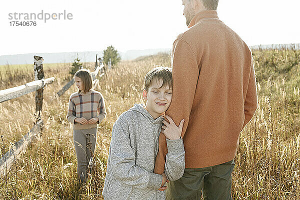 Smiling boy with eyes closed holding hand of father with sister in background