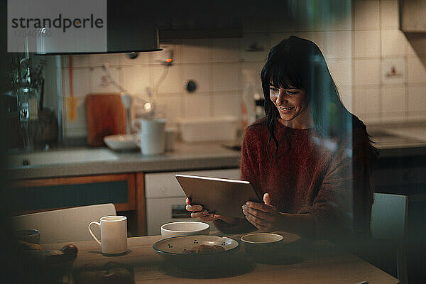 Smiling woman using tablet PC in kitchen