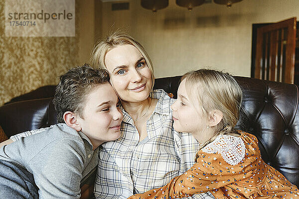 Lächelnde Mutter mit Tochter und Sohn  die zu Hause auf dem Sofa sitzen