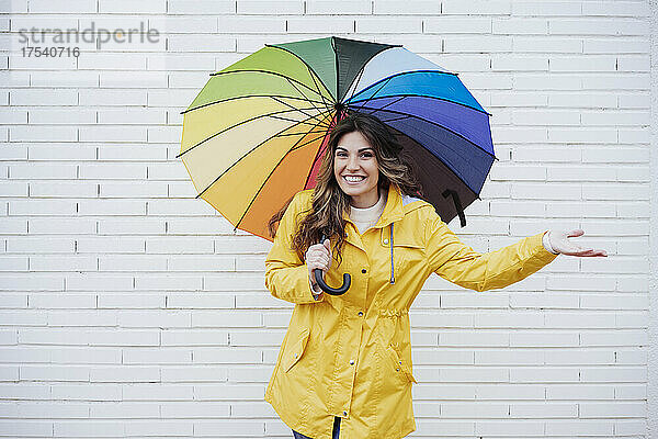 Glückliche Frau steht mit buntem Regenschirm vor der Wand