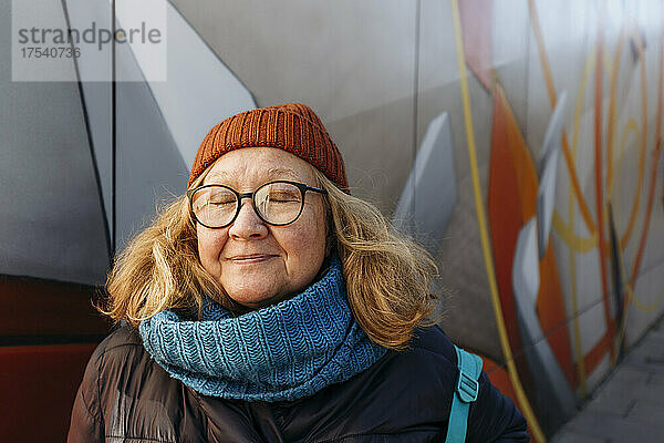 Senior woman with eyes closed in front of wall