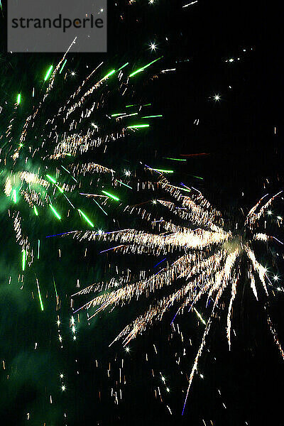 Green and yellow fireworks exploding against clear night sky