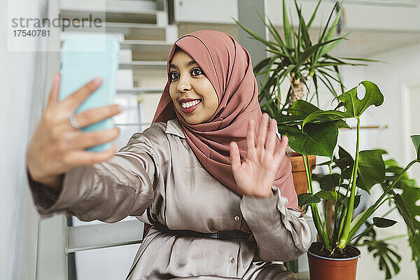 Smiling woman waving on video call through smart phone at home